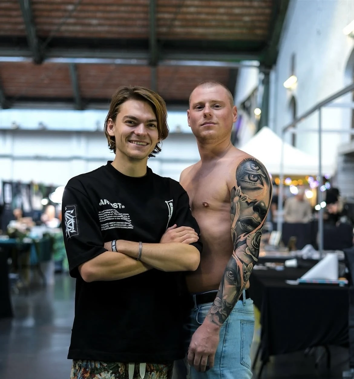 Ravi Brink standing beside a tattooed visitor at an international tattoo convention.