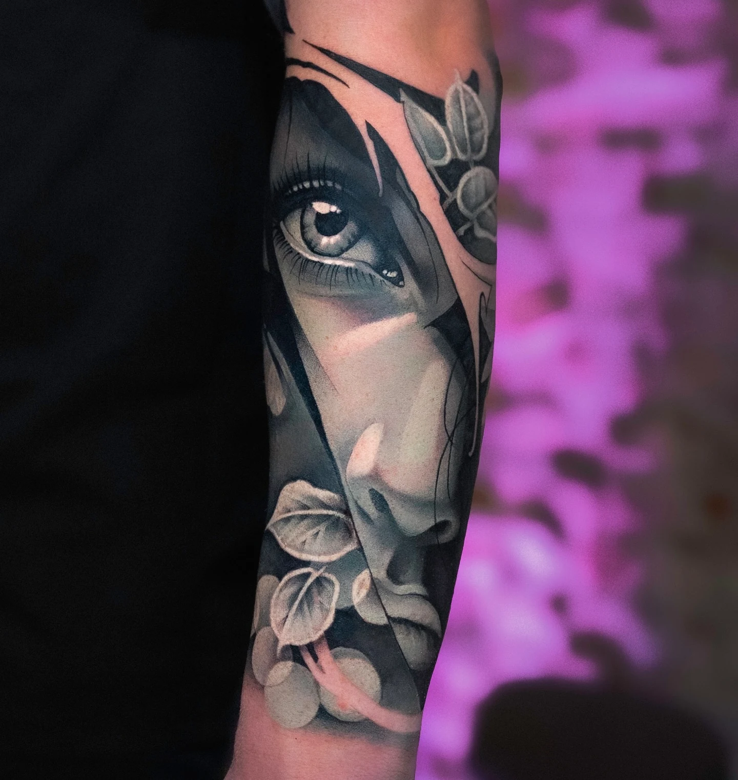 Selective-colour tattoo of a female face and detailed eye surrounded by leaves.